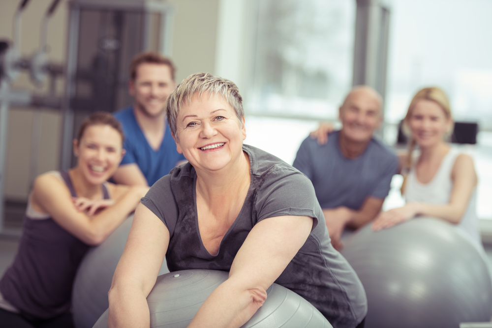 Eine Frau liegt auf einem Gymnastikball. Im Hintergrund sind weitere Personen mit Gymnastikbällen.